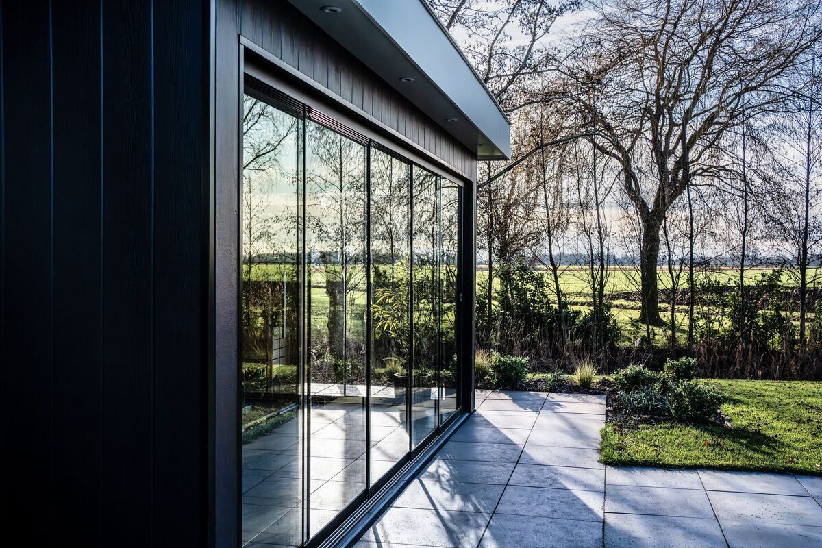Wintergarten mit bodentiefen Glasschiebewänden an einer dunklen Holzfassade