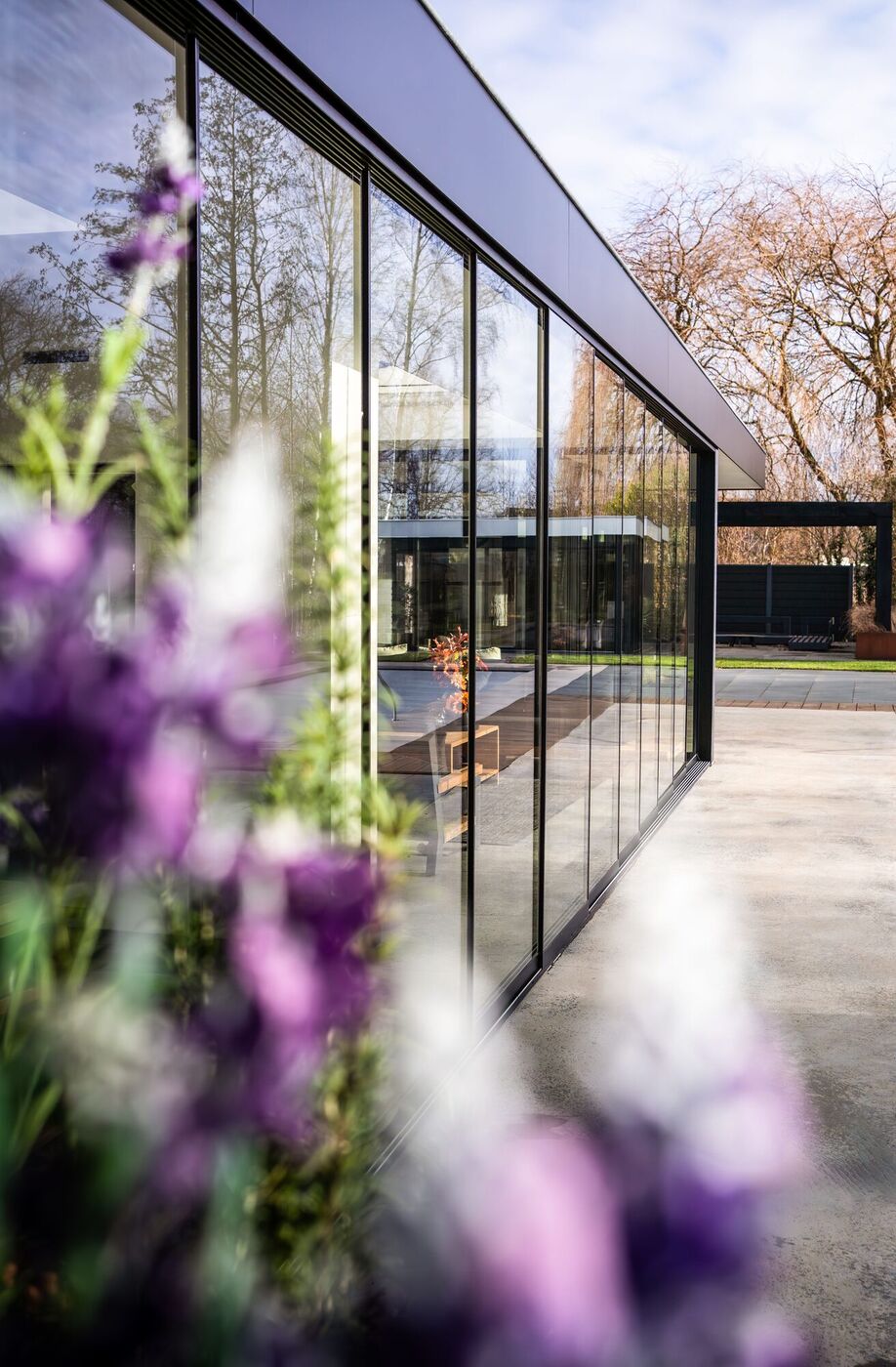 Verglaster Wintergarten mit Aluminiumrahmen an einem Wohnhaus in Moers, im Vordergrund blühende Stauden